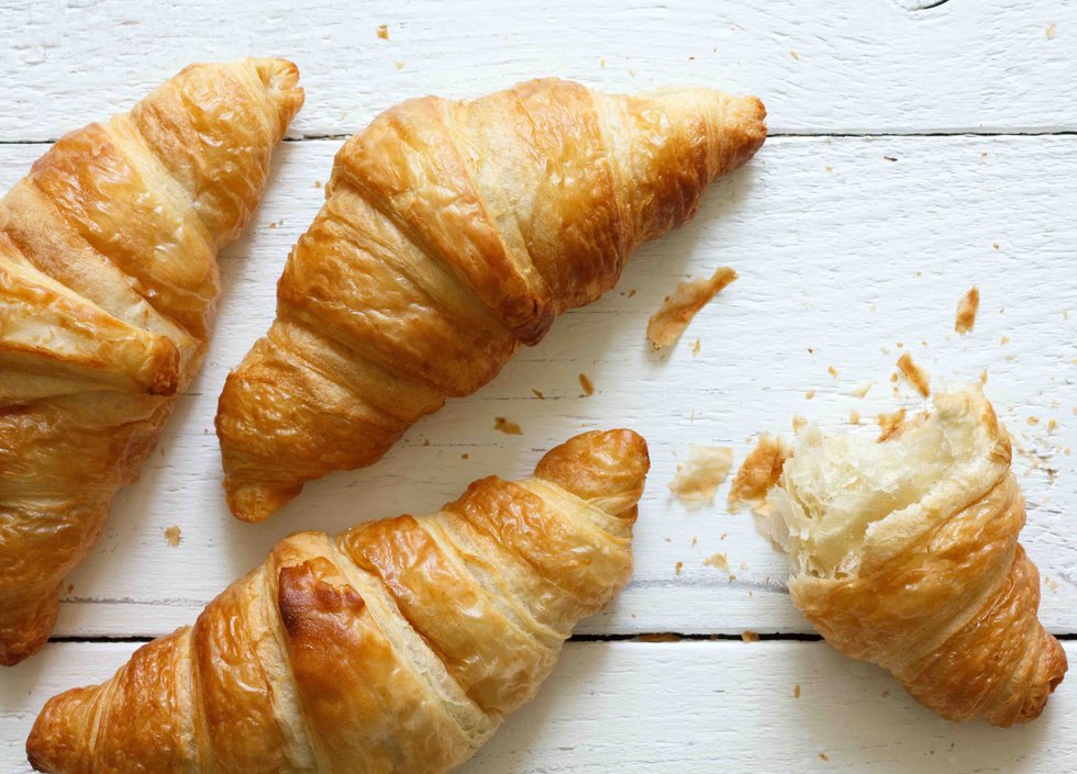 Golden croissants on rustic white wood, from above.